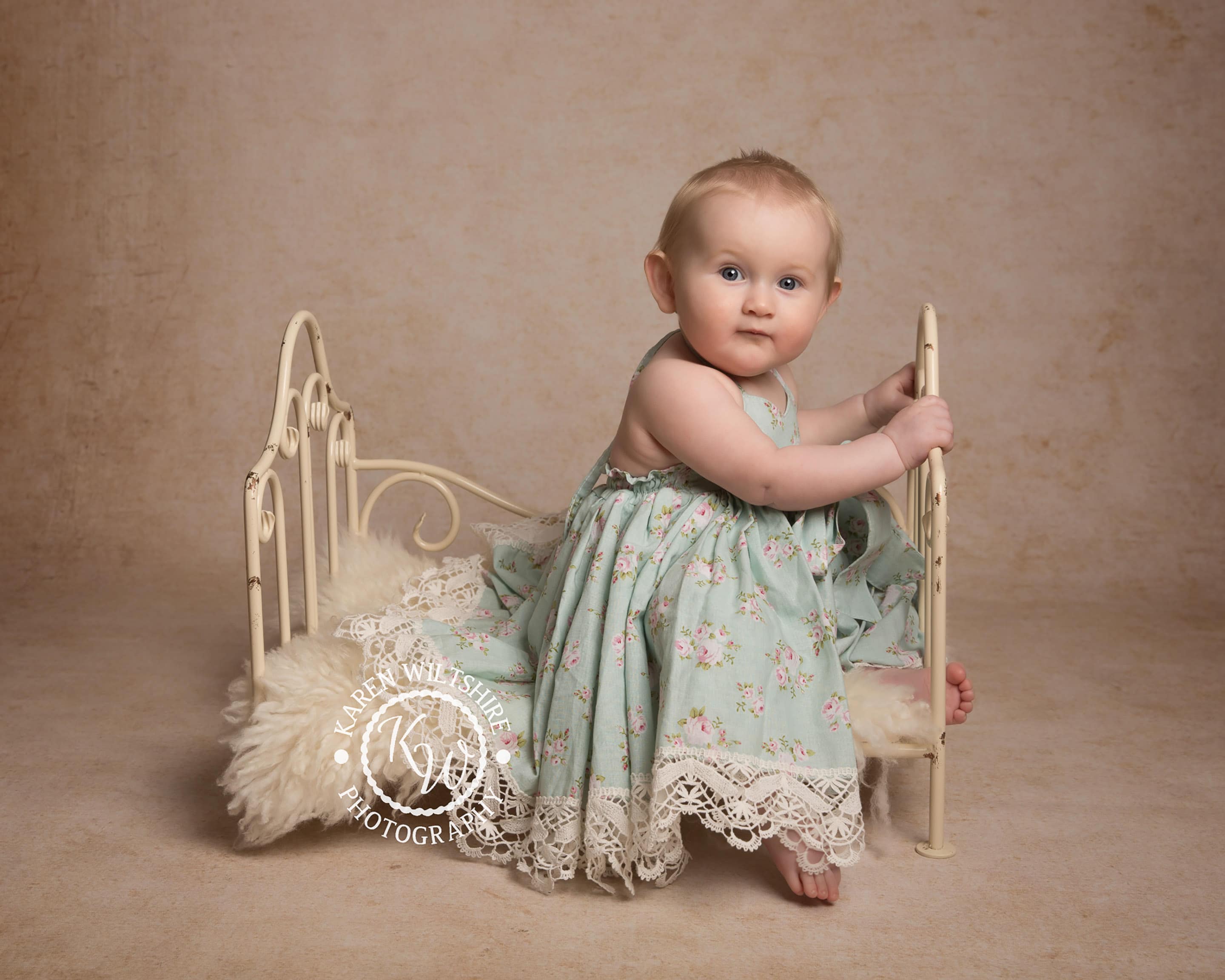 baby in floral dress sitting on metal bed, children & baby photography poole dorset