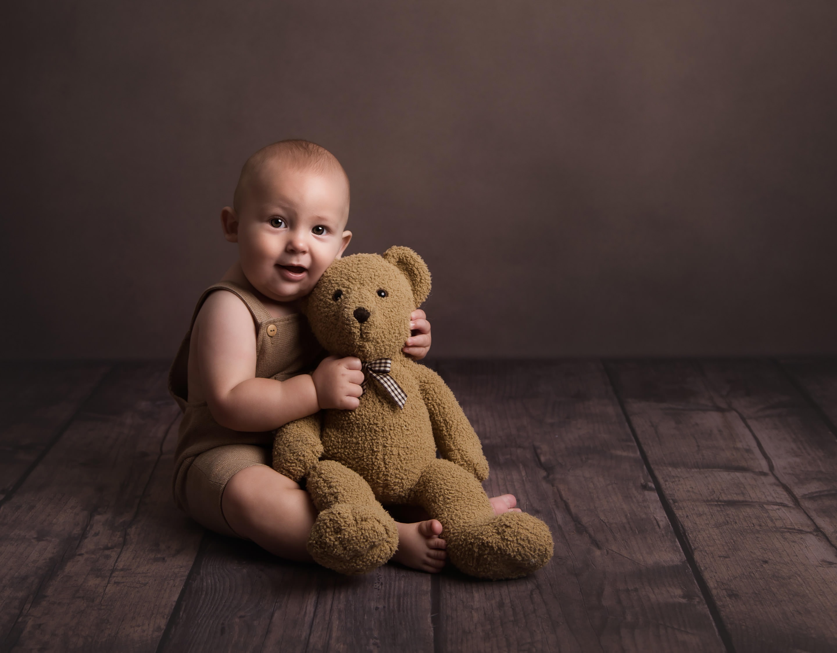 baby sitting on floor cuddling a teddy bear