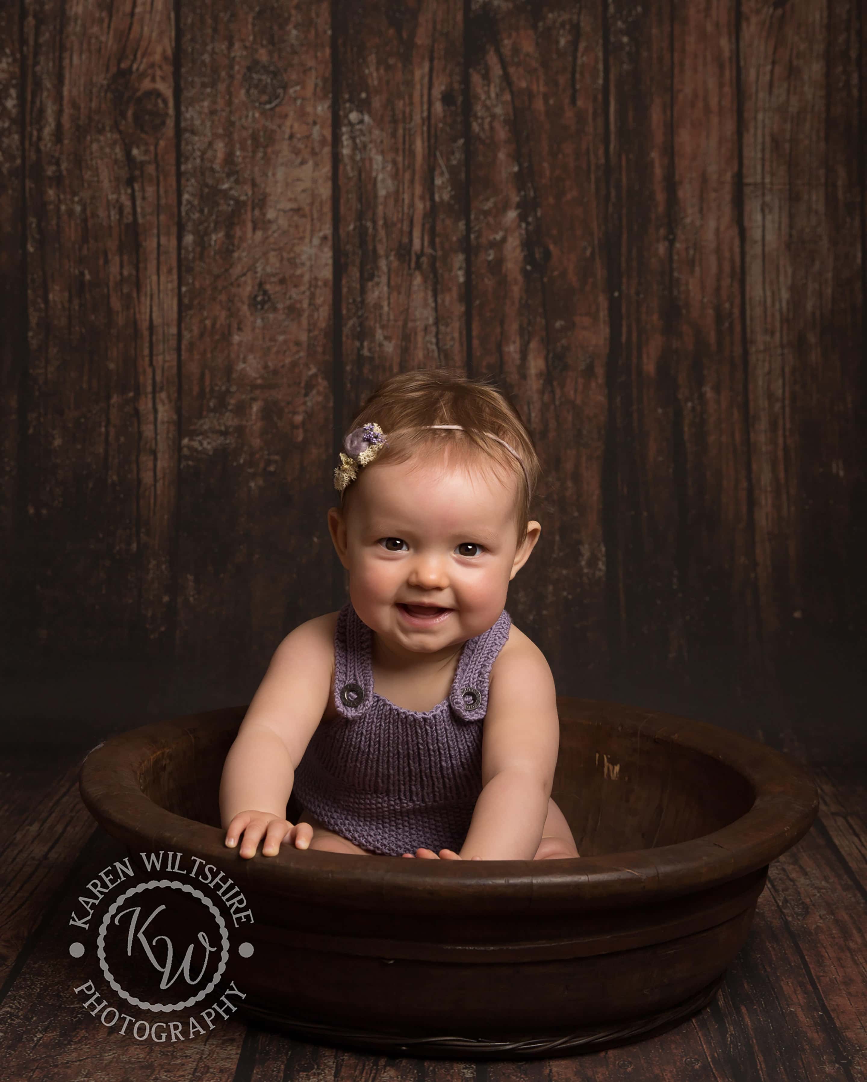 children & baby photography,baby in purple romper sat in a wooden bowl