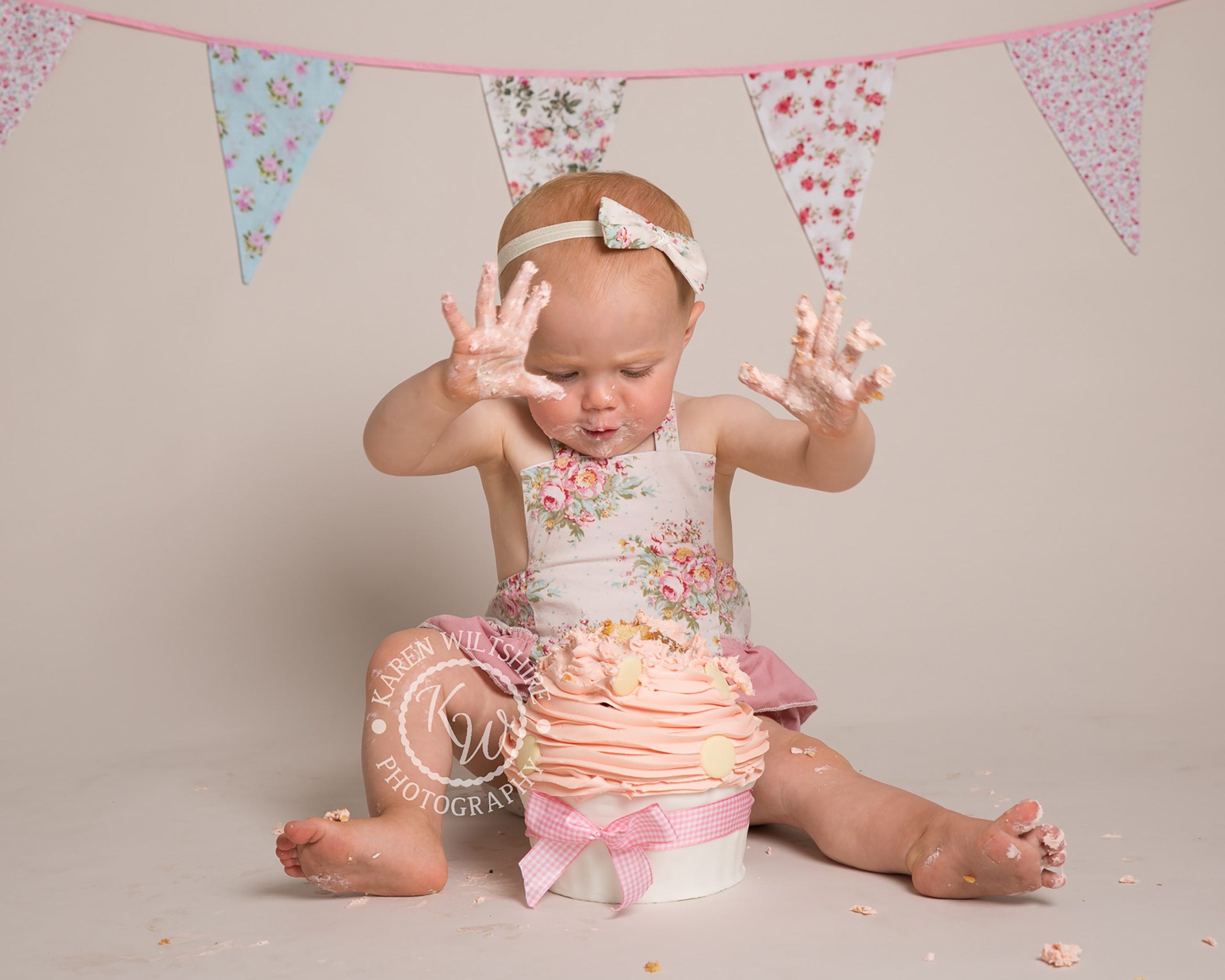 baby girl plunges hands into a giant cup cake