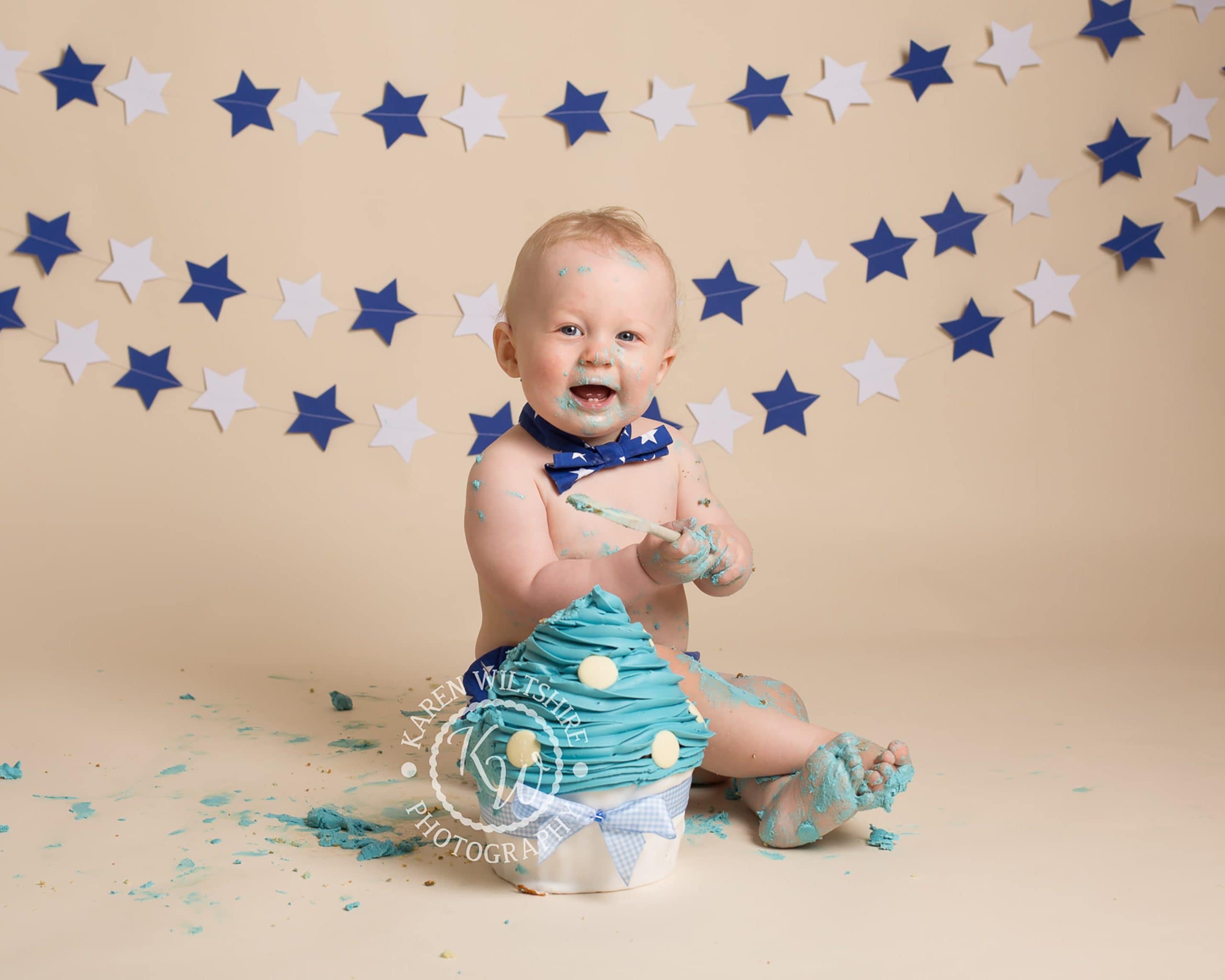 Baby boy enjoying a first birthday photoshoot with a large cupcake to smash