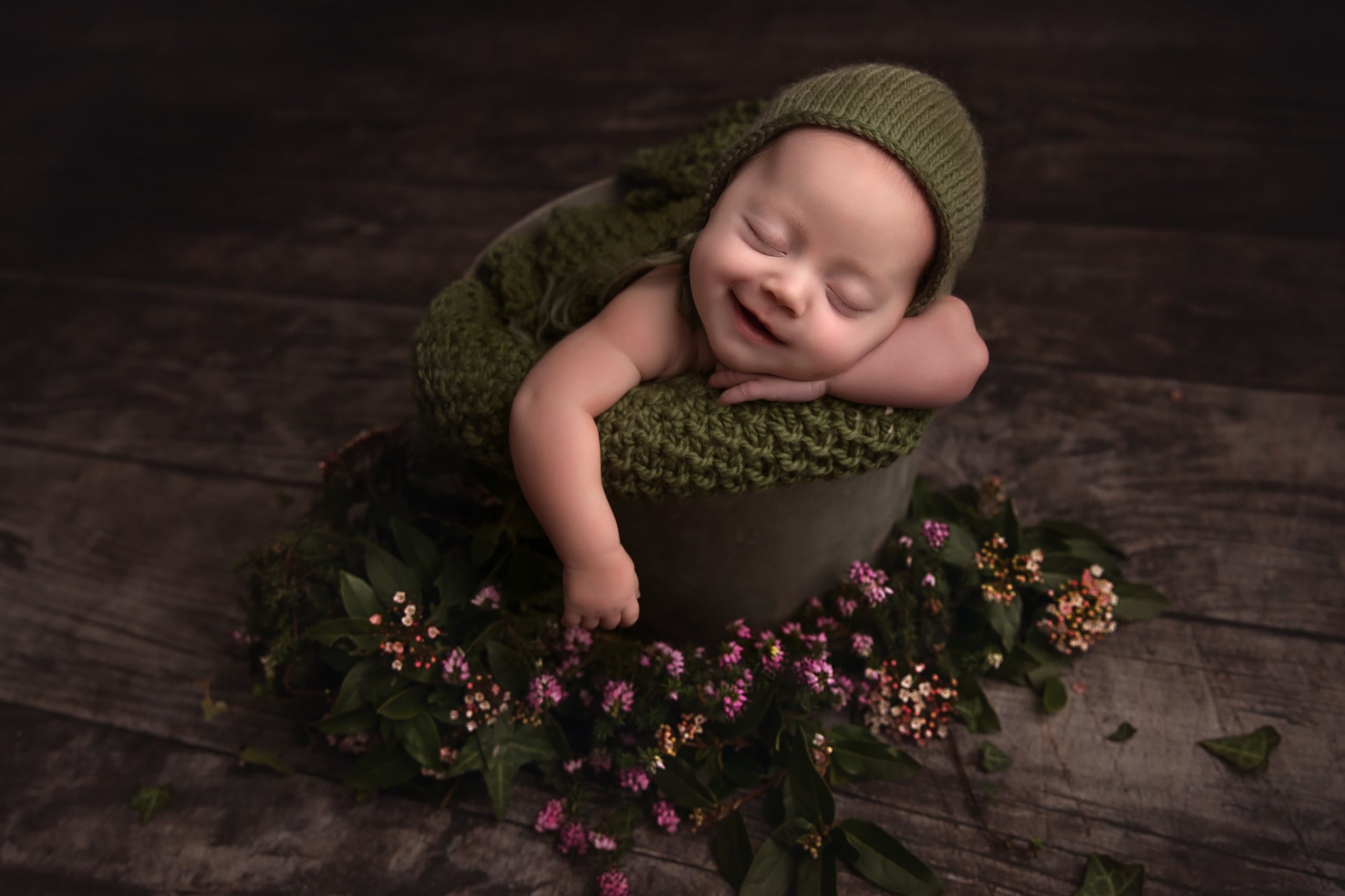 Newborn baby smiling whilst posed in a metal bucket with flowers