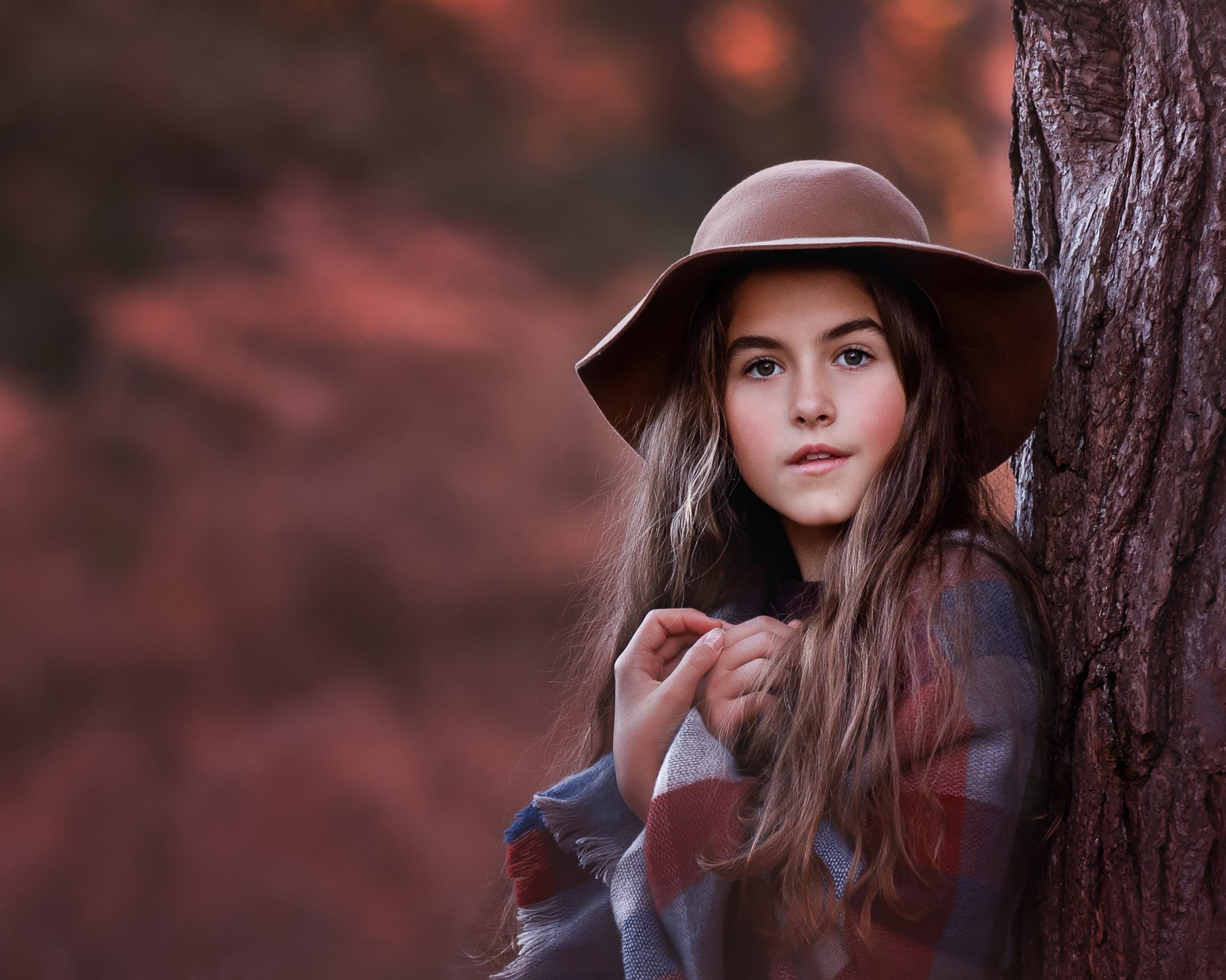 Young girl in hat leaning against a tree in autumn