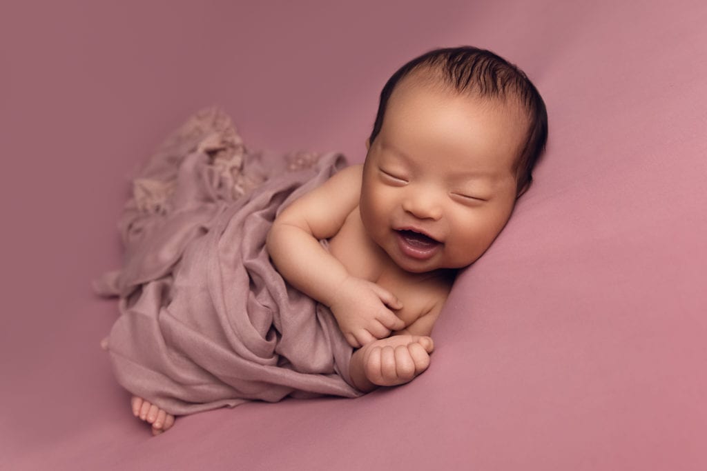 Newborn baby smiling on pink background